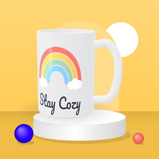 Personalized 15 oz white ceramic mug with a rainbow Stay Cozy design on a yellow studio backdrop